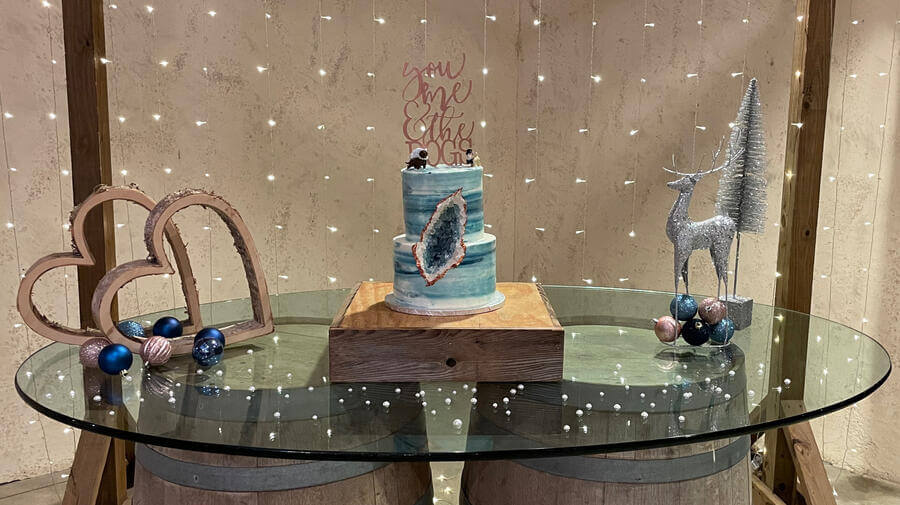Two-tier geode wedding cake on a glass table backed by fairy lights